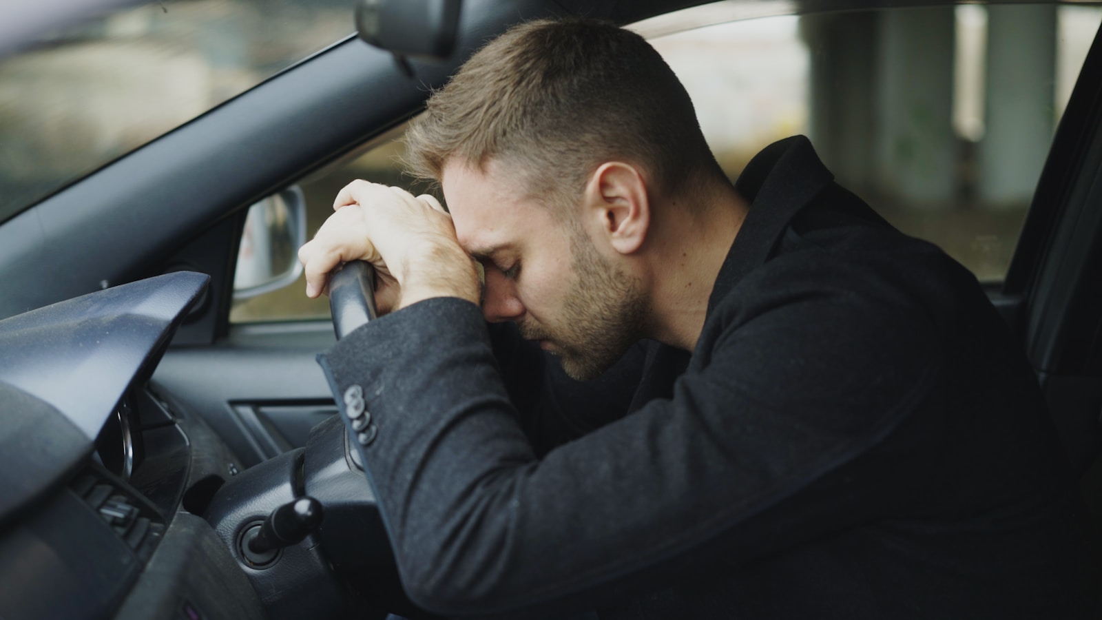 Man resting head on steering wheel in car.