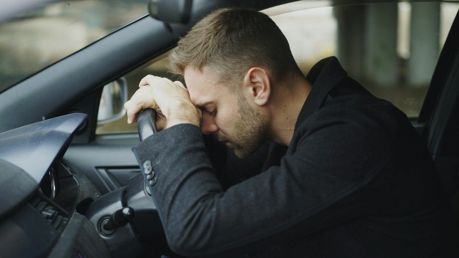 Man resting head on steering wheel in car